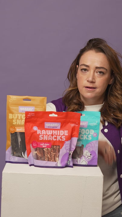 Vrouw legt uit waarom kauwen en kauwsnacks belangrijk zijn voor honden, naast een zuil met drie verpakkingen van Braaaf hondensnacks.